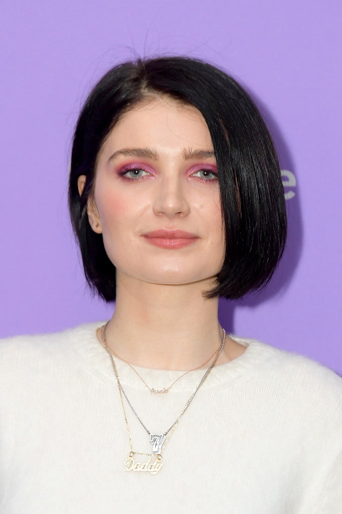 Photo of Eve Hewson wearing a white t-shirt and beautyful ornaments on her neck with purple background